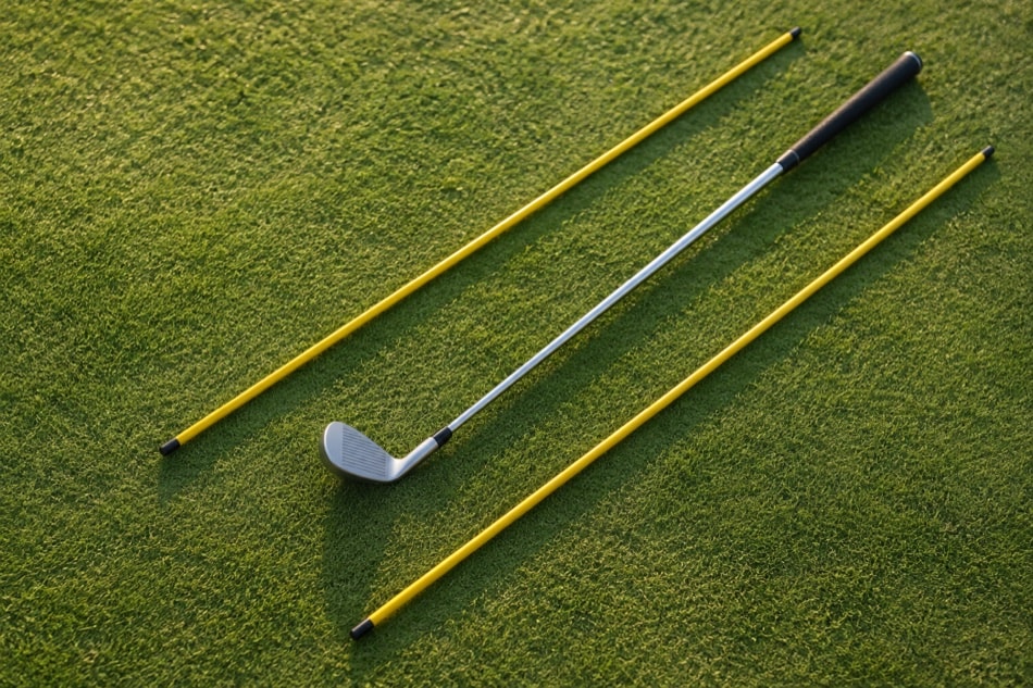 Plain alignment sticks and a club laid on practice grass